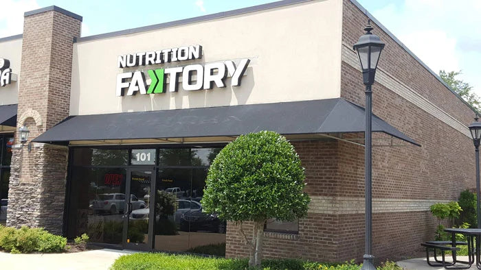 Exterior view of a Nutrition Factory storefront with a black awning and landscaping.